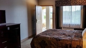 Ein Hotelzimmer mit Bett, einem Schminktisch, einem Fernseher und einem Fenster mit Vorhängen.