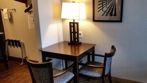 A hotel room with a wooden table, two patterned chairs, a standing heater, and a framed picture on the wall. - Your Budget-Friendly Home Away from Home l 2 Queen Beds Suite (Beeville)