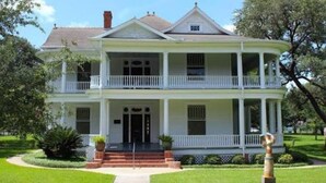 A two-story house with a front porch, a central entrance, and a symmetrical facade. - Your Budget-Friendly Home Away from Home l 2 Queen Beds Suite (Beeville)