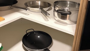 Een keuken met een wit aanrecht, een zwarte koekenpan en roestvrijstalen kookgerei.