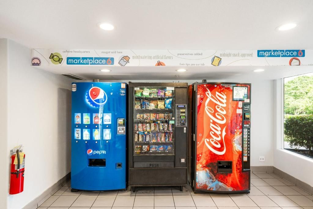 Three beverage vending machines in a room with tiled flooring and a window.