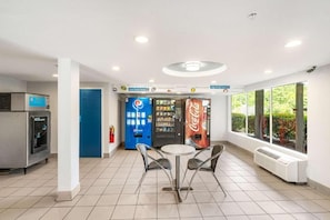 Un espacio interior limpio y bien iluminado con máquinas expendedoras, una mesa con sillas y ventanas amplias.