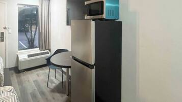 A compact room with a refrigerator, a microwave on top, a small table, and a chair.