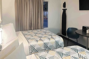 Habitación de hotel con cama, una silla, una mesa, ventana con cortinas y un objeto fijado a la pared.
