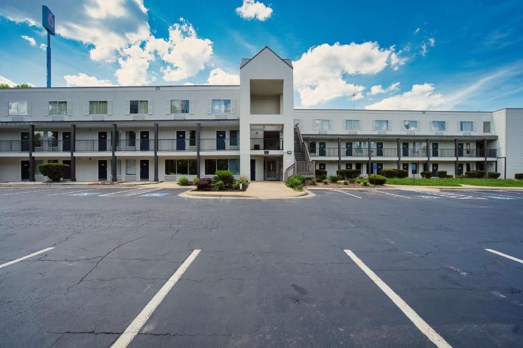 A multi-story motel with a central entrance, parking lot, and a clear sky.