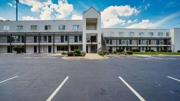A multi-story motel with a central entrance, parking lot, and a clear sky.