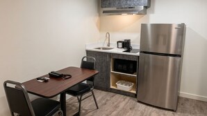 Une cuisine compacte équipée d’un réfrigérateur en acier inoxydable, d’un four à micro-ondes et d’une machine à café posés sur le plan de travail.