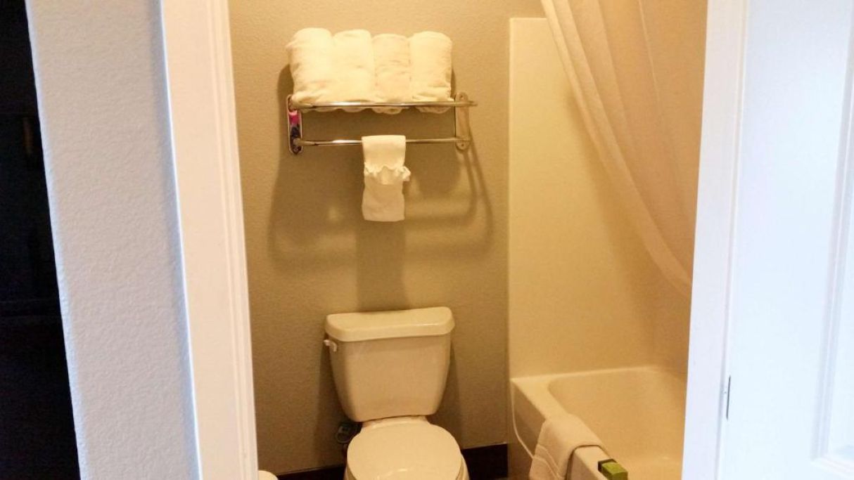 A bathroom with a toilet, a towel rack with towels, and a bathtub.