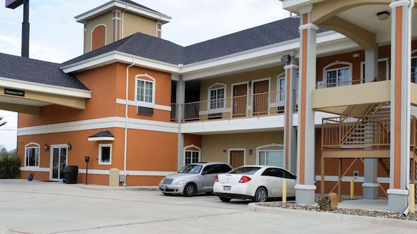 A multi-story hotel with a parking area, two cars parked, and a clear sky.