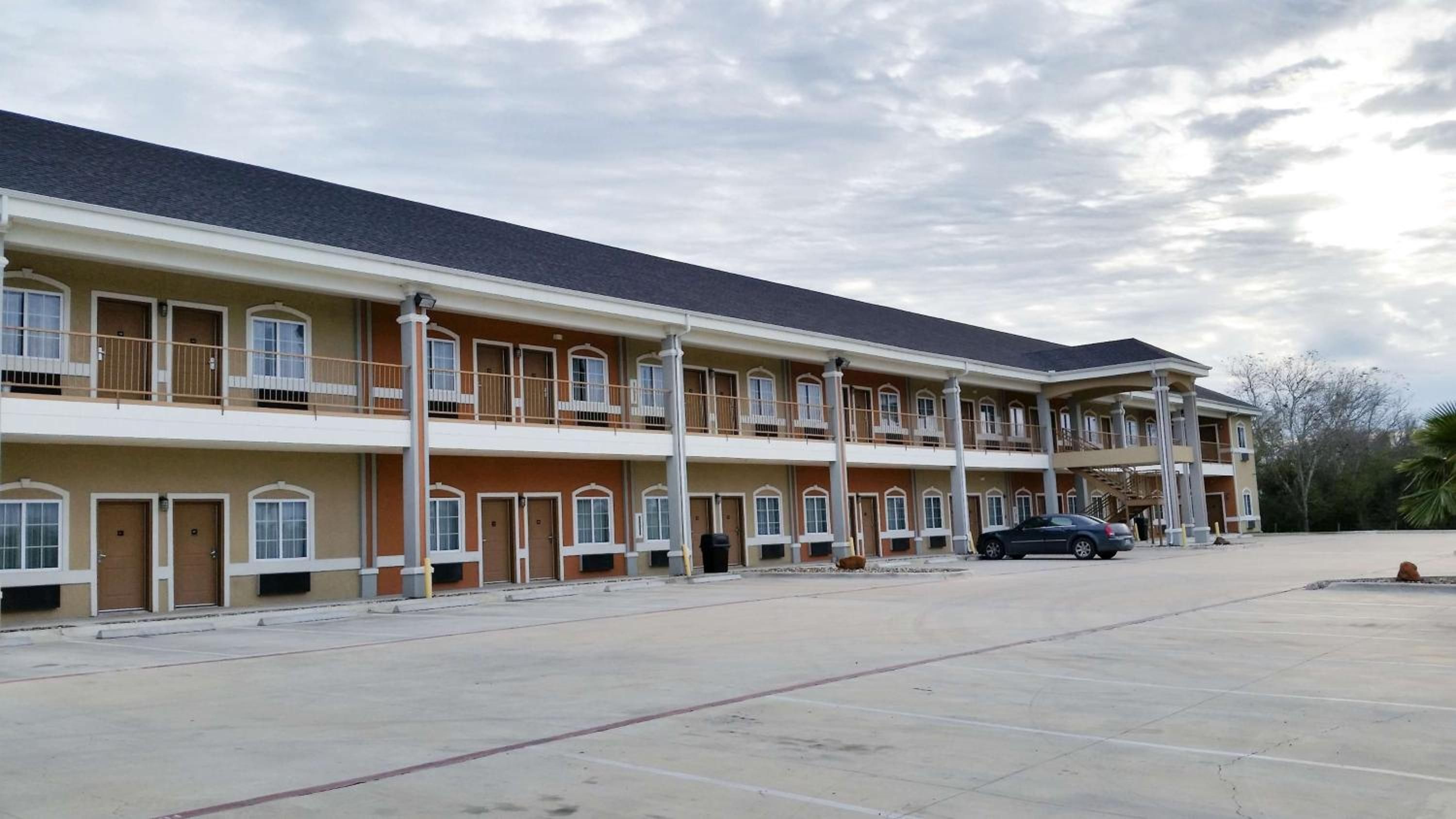 Un hotel de varios pisos con una fila de habitaciones en cada planta, una zona de estacionamiento techada y un automóvil en el estacionamiento.
