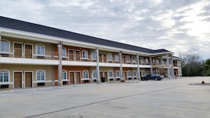 Un hôtel à plusieurs étages, avec une rangée de chambres à chaque étage, un parking couvert et une voiture stationnée sur le parking.