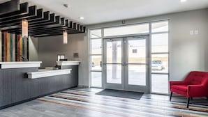 Un'area reception dal design moderno, con una scrivania, una sedia rossa e un'ampia porta in vetro che dà sull'esterno.