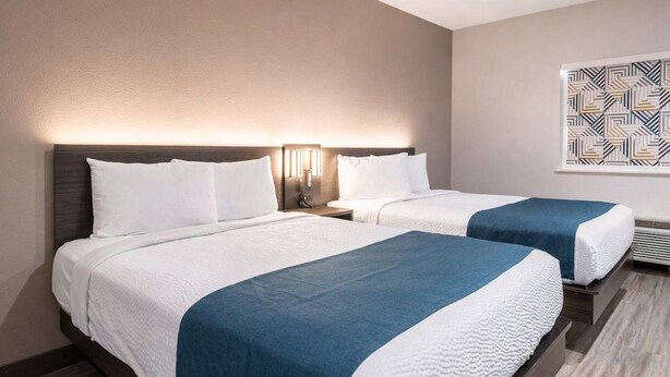 Una camera d'albergo con due letti, ognuno con biancheria bianca e un tocco di blu.