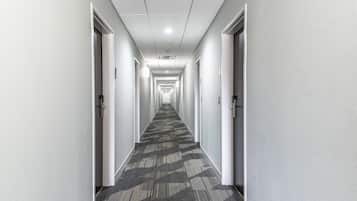 Un largo y estrecho pasillo con pisos alfombrados y paredes blancas, que conduce a varias puertas.