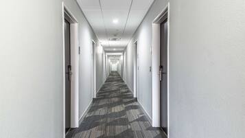 Un largo y estrecho pasillo con pisos alfombrados y paredes blancas, que conduce a varias puertas.