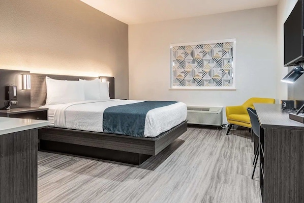 A modern hotel room with a bed, bedside table, lamp, air conditioning unit, and a yellow chair.