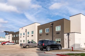 A modern multi-story hotel with a parking lot, featuring a flat roof design and large windows.
