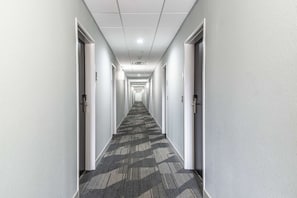 A long, narrow hallway with carpeted floors and white walls, leading to multiple doors.