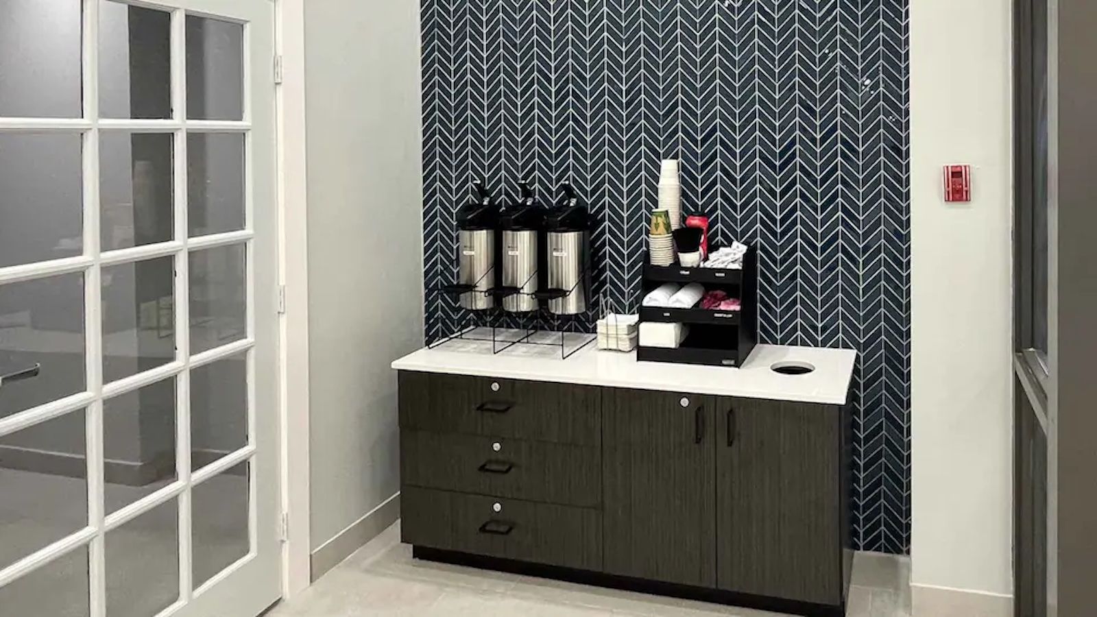 Une chambre dotée d’un mini-bar, d’une porte avec des panneaux en verre dépoli et d’un papier peint à motifs.