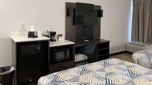 A hotel room with a kitchenette, a TV mounted on the wall, a desk, a chair, and two beds with patterned bedding. - Queen Room w/ Kitchenette| Free Parking | 4.8 Miles from Lamp-Lite Theatre (Nacogdoches)