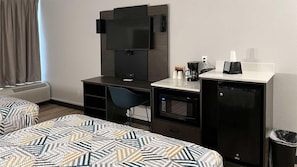 Une chambre d’hôtel avec deux lits, un bureau, une chaise, une télévision, un four à micro-ondes et une machine à café.