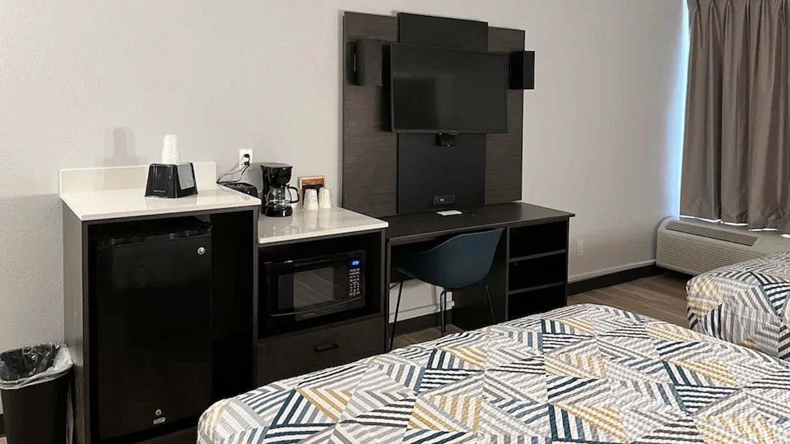 Une chambre d’hôtel équipée d’une kitchenette, d’un téléviseur fixé au mur, d’un bureau, d’une chaise et de deux lits avec une literie à motifs.