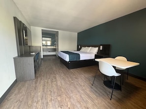 Een slaapkamer met een bed, een bureau en een stoel. Er hangt een spiegel aan de muur en een deur die naar een andere kamer leidt.