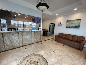 A lobby with a reception desk, a brown leather sofa, a patterned rug, and a painting on the wall.