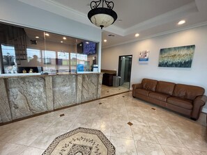 A lobby with a reception desk, a brown leather sofa, a patterned rug, and a painting on the wall.