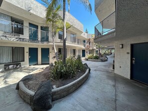 A courtyard with a central planter, a palm tree, and a building with balconies and doors numbered 220 and 203.