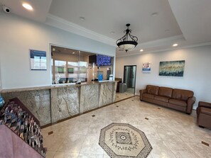 A lobby with a reception desk, a brown leather sofa, a patterned rug, and a ceiling light fixture.