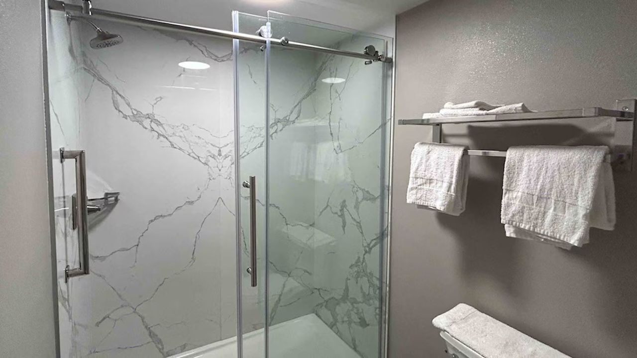 A bathroom with a glass shower enclosure, a marble wall, and a towel rack with towels.
