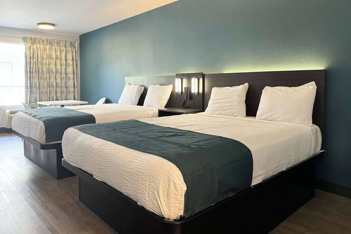 A hotel room with two beds, a desk, and a large window with curtains.