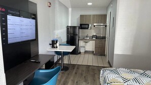 A compact hotel room with a TV displaying a channel guide, a small dining table with chairs, a kitchenette, and a bed. - Budget-Friendly Room w/ Kitchen | 3 Miles to Downtown | Free Parking | Pets OK (West Palm Beach)
