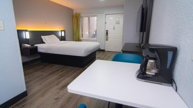 A hotel room with a bed, a desk, a chair, a coffee maker, a TV, and a door with a window. - Budget-Friendly Room w/ Kitchen | 3 Miles to Downtown | Free Parking | Pets OK (West Palm Beach)
