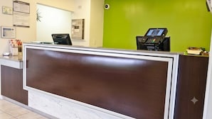 Vastaanottotiski, jossa on digitaalinen infopiste, marmorilaatoitettu lattia ja vihreä seinä.