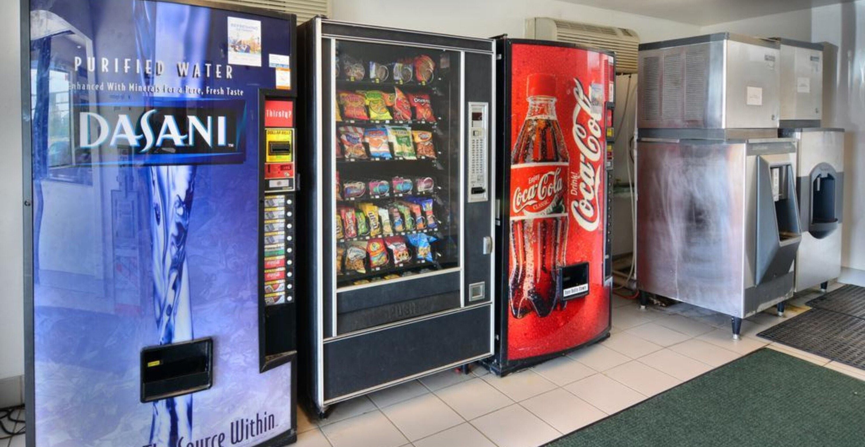 Zona de máquinas expendedoras con dispensador de agua Dasani, máquina de aperitivos y refrigerador de Coca-Cola.