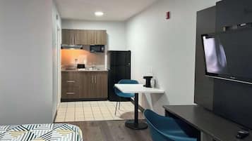 Habitación de hotel compacta con kitchenette, una cama con ropa de cama estampada, un televisor y un pequeño comedor.