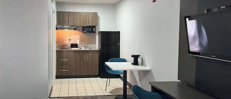 A compact hotel room with a kitchenette, a bed with patterned bedding, a TV, and a small dining area.