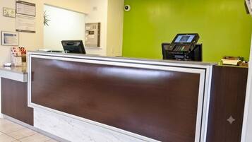 Una recepción con mostrador, quiosco digital, suelo de baldosas de mármol y pared verde.