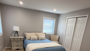 Un dormitorio con cama, mesita de noche, lámpara, ventana y armario.