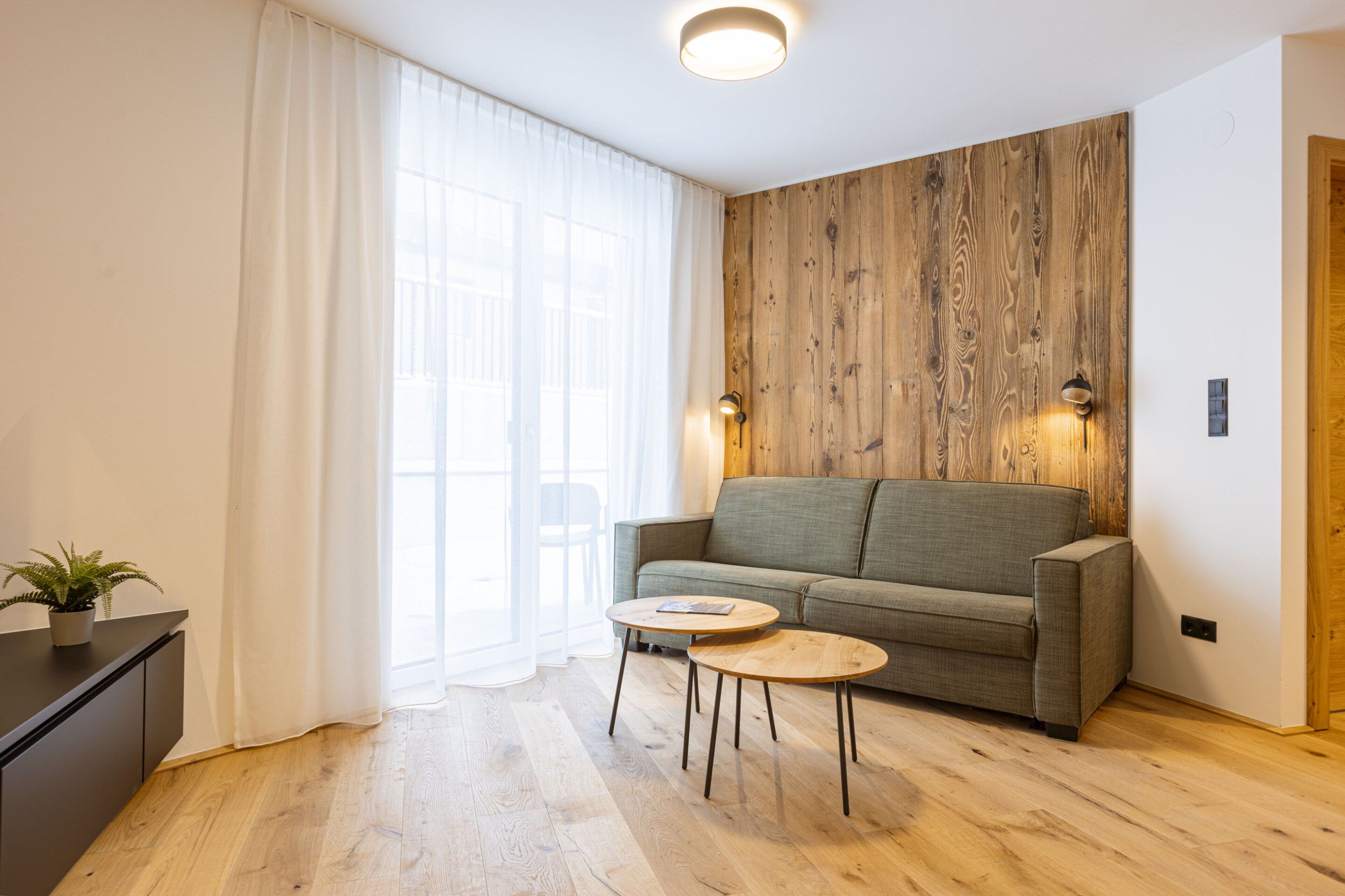 A modern living room with a wooden accent wall, a grey sofa, a small round table, and a potted plant.