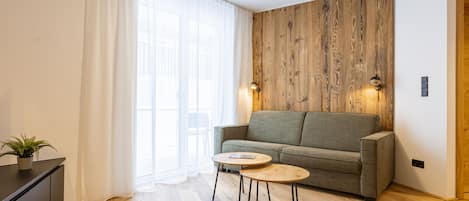 A modern living room with a wooden accent wall, a grey sofa, a small round table, and a potted plant.