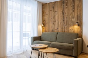 Ein modernes Wohnzimmer mit einem grauen Sofa, zwei runden Holztischen und einer Wand im Holzstil.