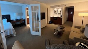 A hotel room with a bed, a desk, a chair, a sofa, a dining table, and a kitchenette area. - Northwell All Suite Hotel (Toronto)