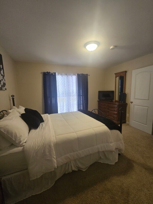 A bedroom with a bed, a dresser, a television, and a door.