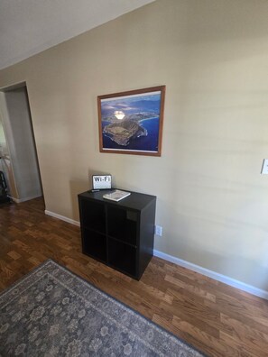 A room with a wooden floor, a black entertainment unit with a Wi-Fi sign, a framed landscape painting, and a patterned rug.