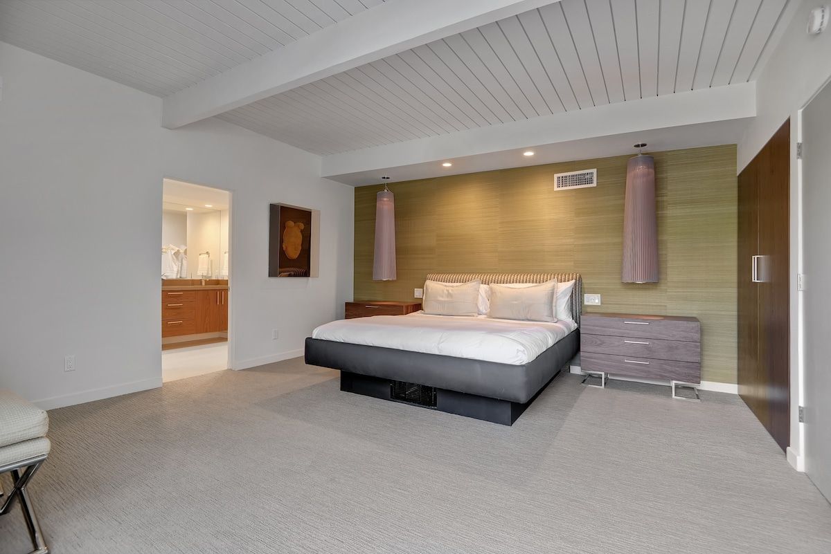 Un dormitorio moderno con una cama grande, una mesita de noche, un aparador y un armario empotrado.