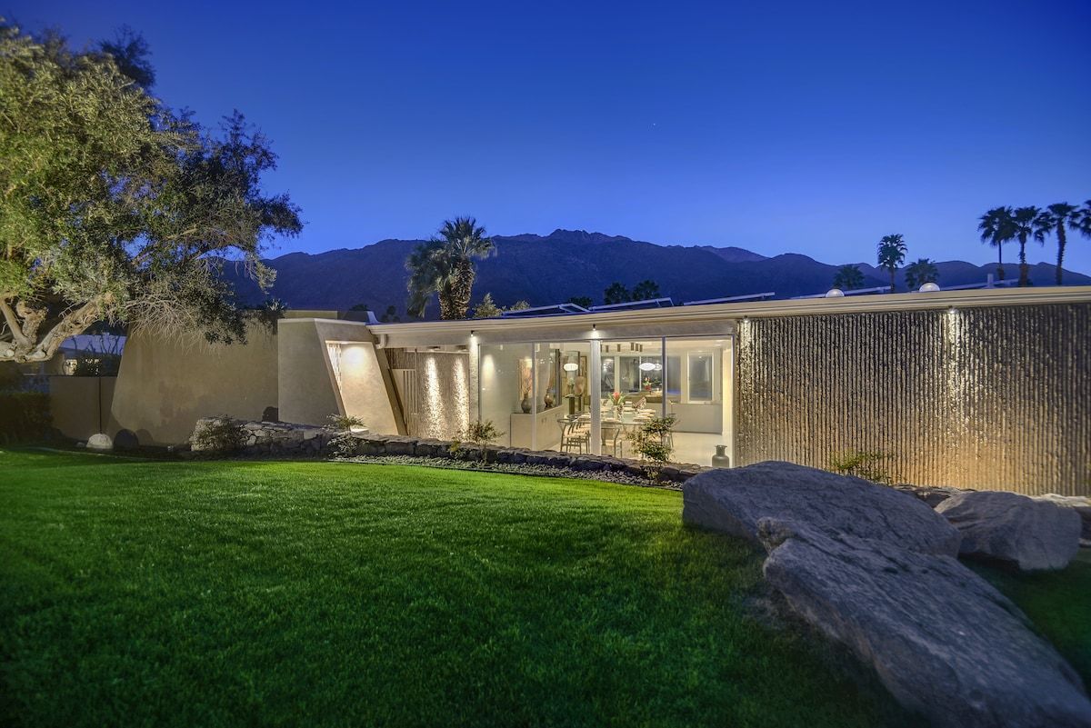 Une maison moderne avec une pelouse bien entretenue, de gros rochers et une chaîne de montagnes en arrière-plan.