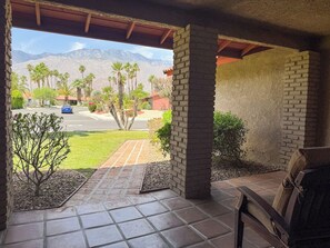 A covered patio with a view of a street, palm trees, and mountains in the distance. - Vista El Quetzal - Central Palm Springs (Palm Springs)